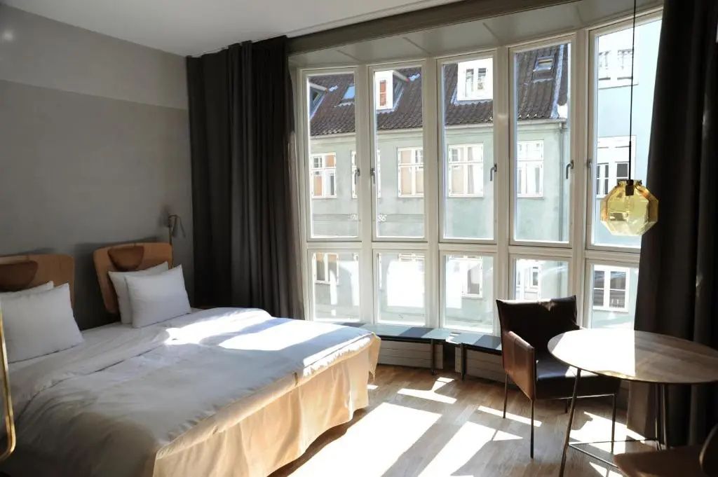 Sonniges Hotelzimmer mit Doppelbett und großen Fenstern zur Stadt