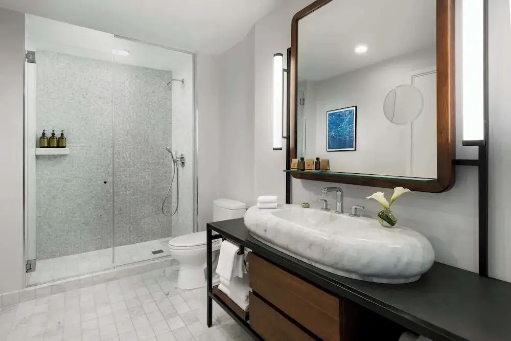 Modernes Badezimmer mit ovalem Marmorwaschbecken, großem Spiegel, Toilette und glasabtrennter Dusche.