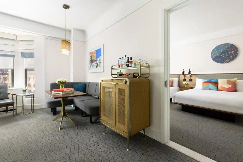 Sitzbereich einer Suite mit Ecksofa, Beistelltisch, Servierwagen und Blick in das Schlafzimmer.
