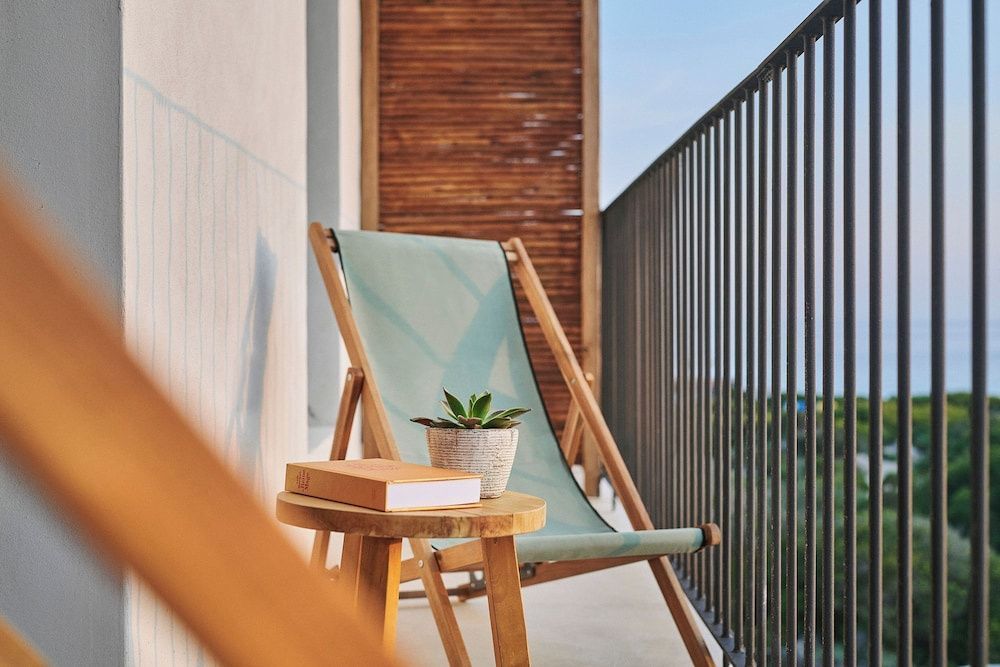 Balkon mit hellblauem Klappstuhl, Beistelltisch aus Holz und Pflanze am Geländer.