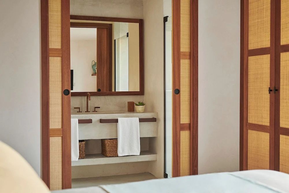 Blick durch geöffnete Schiebetüren auf den Waschtisch und Spiegel im Badezimmer.
