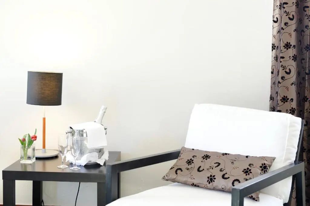 Sessel mit Zierkissen und Beistelltisch samt Sektkühler und Gläsern im Hotelzimmer.