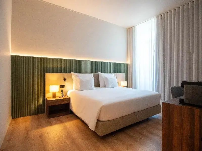 Hell eingerichtetes Hotelzimmer mit Doppelbett, grüner Akzentwand und Parkettboden.
