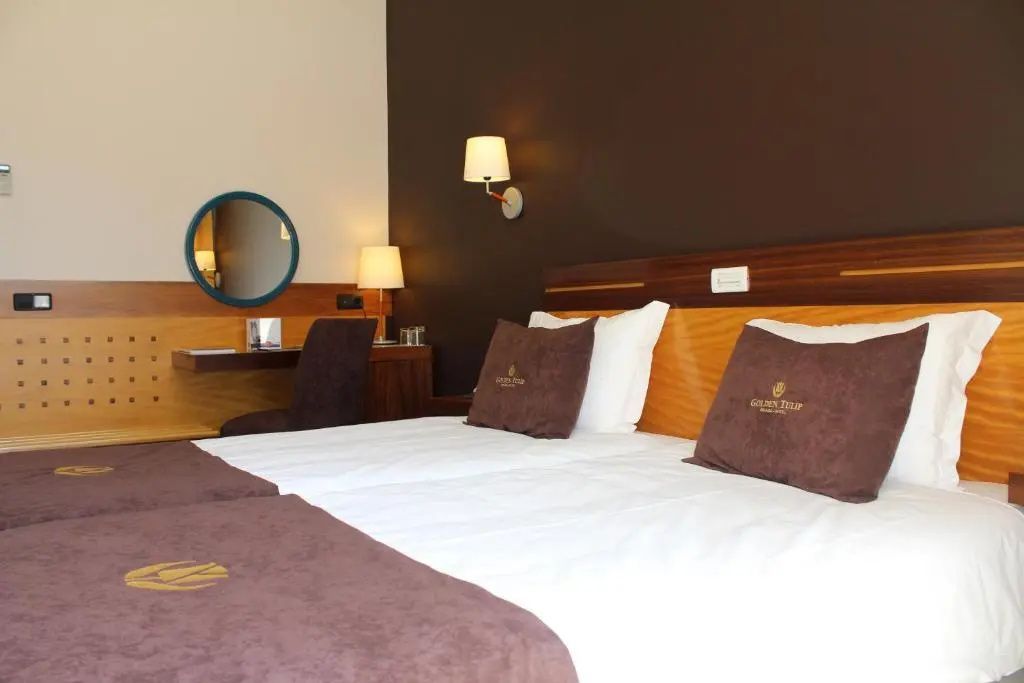 Doppelbett mit braunen Kissen und dunkler Wandverkleidung im Hotelzimmer.