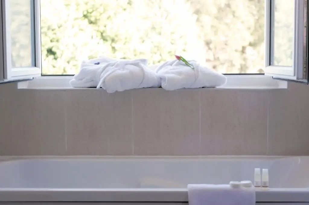 Zwei zusammengelegte weiße Bademäntel liegen auf einer Ablage über der Wanne.