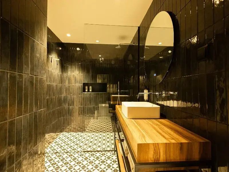 Modernes Badezimmer mit dunklen Wandfliesen, Waschtisch aus Holz und einer begehbaren Dusche.
