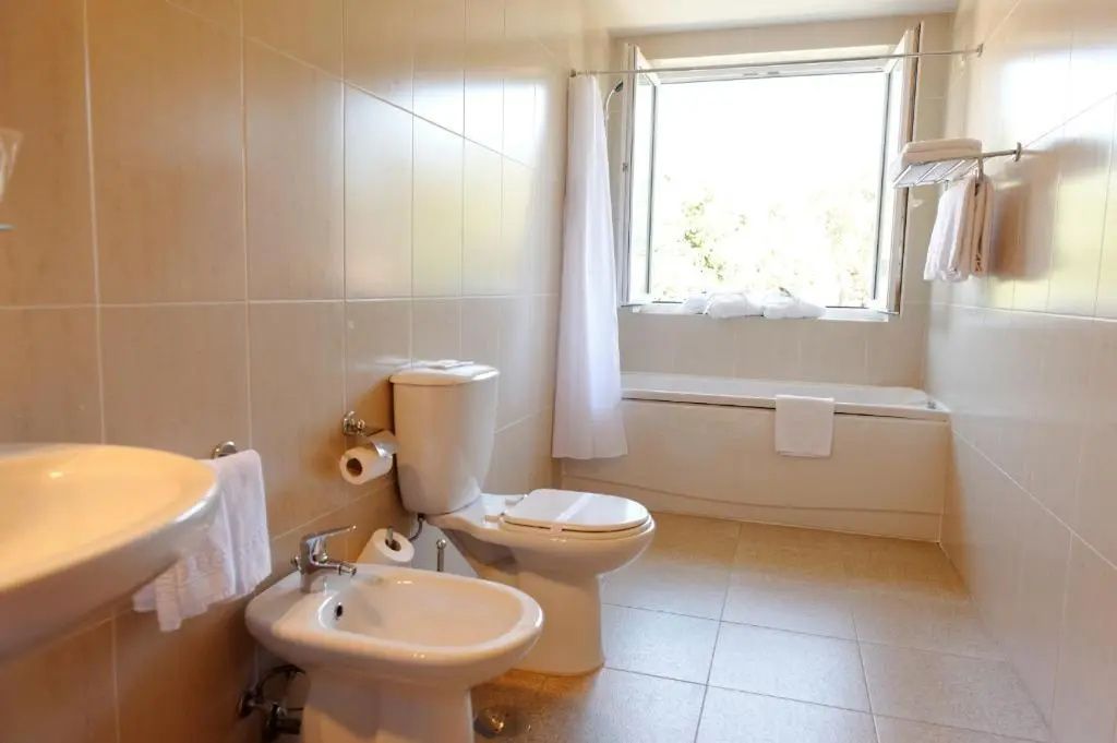 Hell gefliestes Badezimmer mit Toilette, Bidet, Badewanne und Fenster.