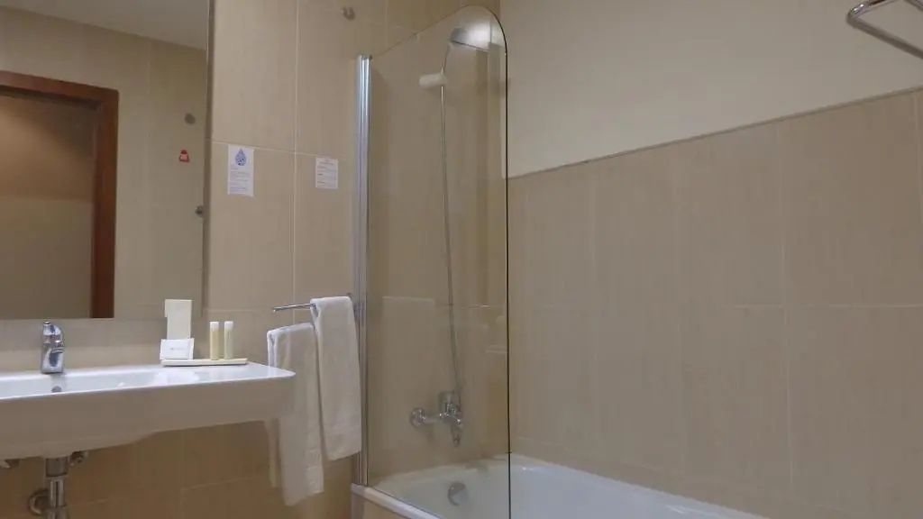 Badewanne mit Duschglaswand und Waschbecken in hell gefliestem Badezimmer.