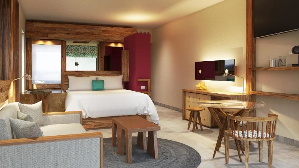 Helles Hotelzimmer mit großem Doppelbett, Holzmöbeln, rundem Teppich und Sitzgelegenheiten.
