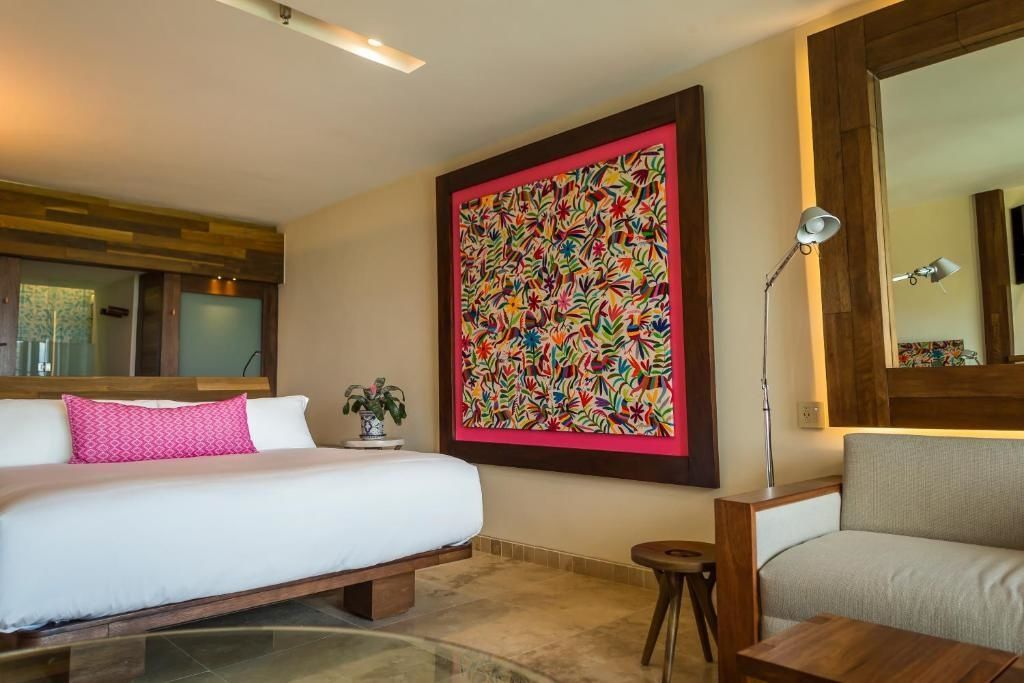 Hotelzimmer mit buntem Wandbild, Bett mit rosa Kissen und hölzernem Beistelltisch.