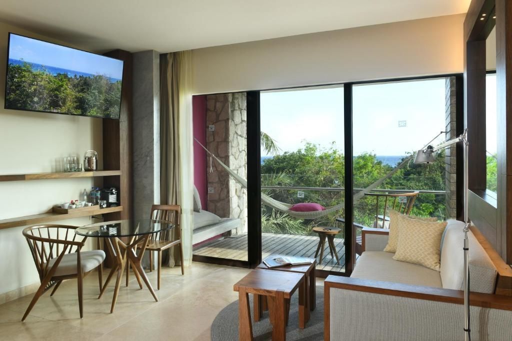 Wohnbereich im Zimmer mit Esstisch, Sofa und Blick durch die Balkontür ins Grüne.