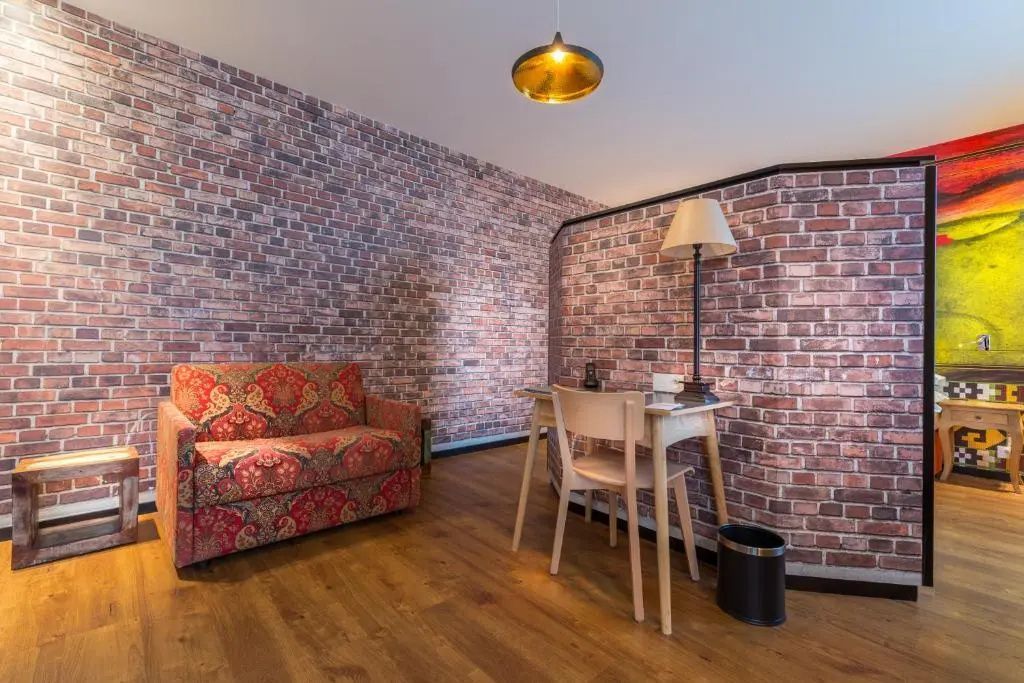 Sitzbereich in einem Zimmer mit Backsteinwand, gemustertem Sofa und Schreibtisch.