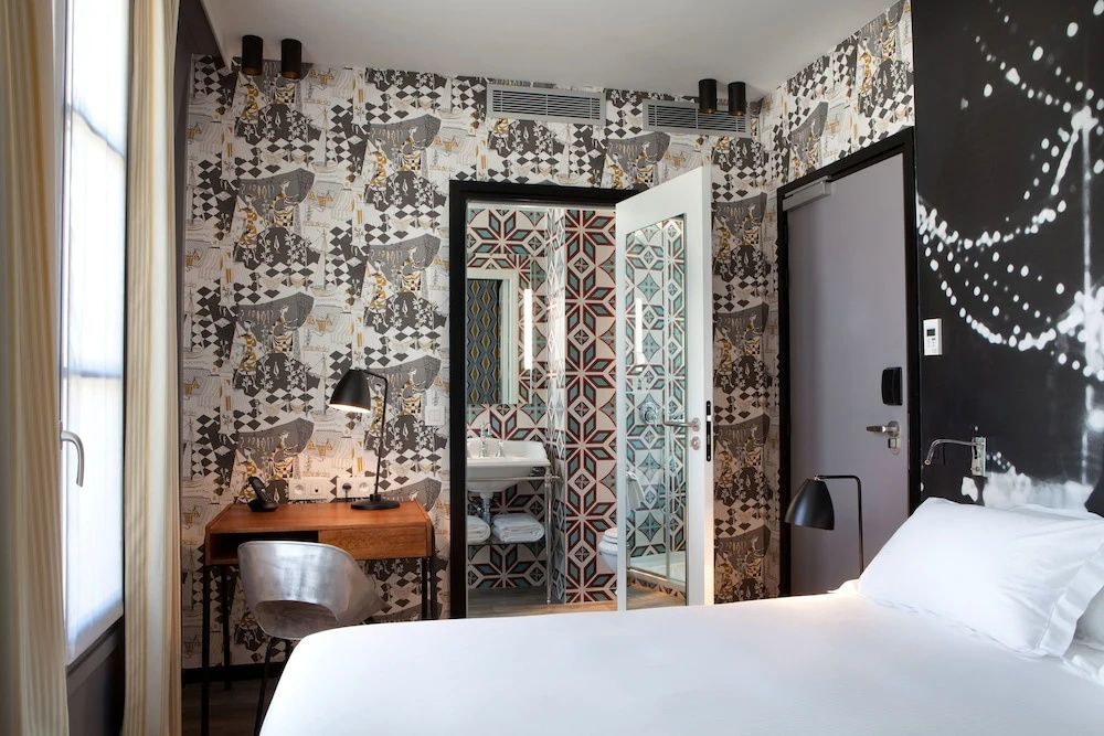 Blick durch ein Hotelzimmer auf einen Schreibtisch und die offene Tür zum Badezimmer.
