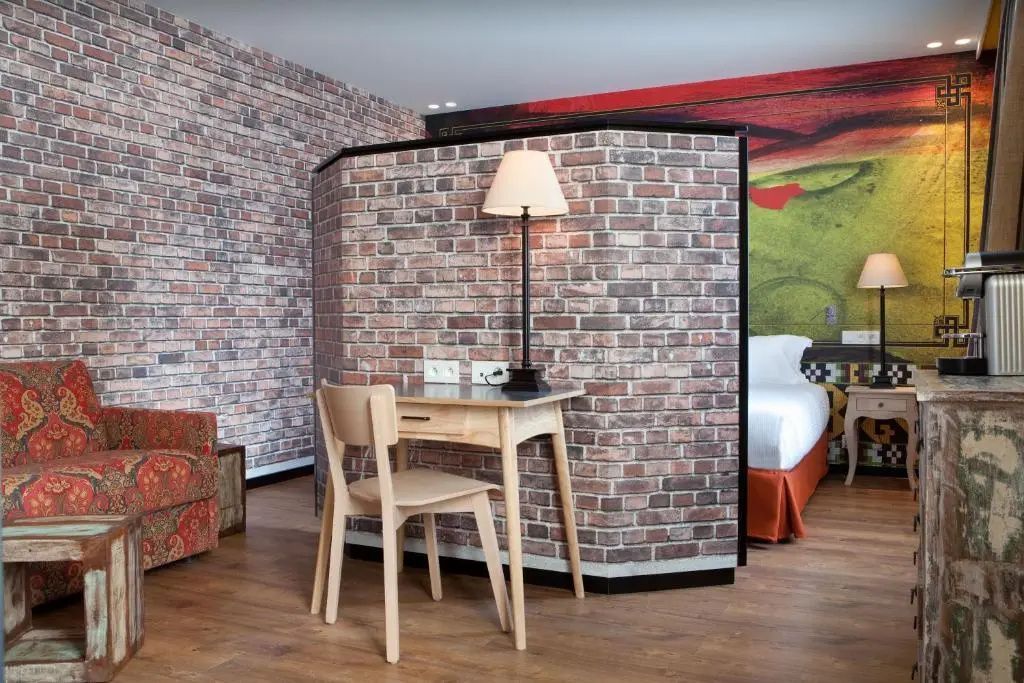 Hotelzimmer mit Backsteinoptik an der Trennwand sowie Schreibtisch und Holzboden.