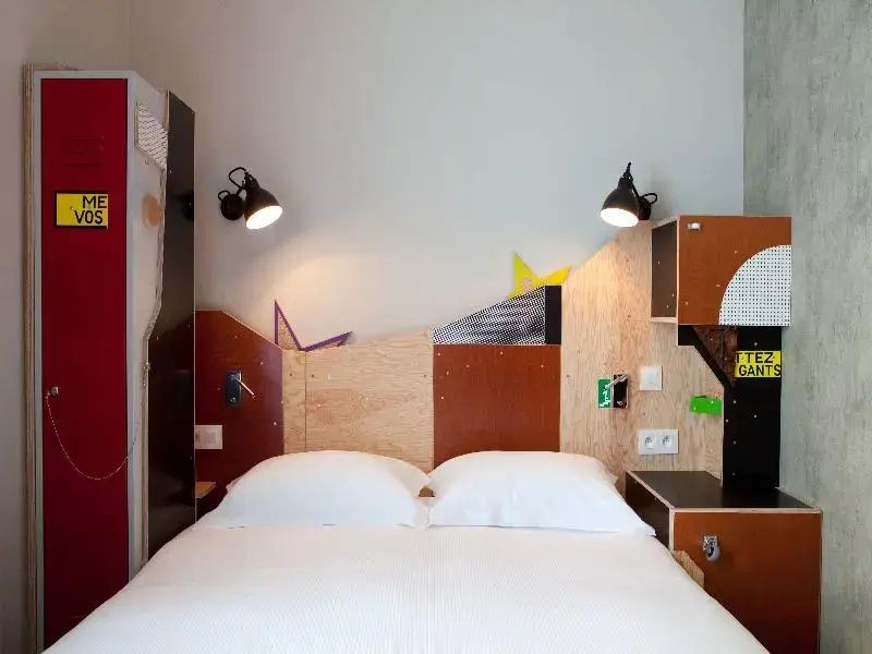 Doppelbett mit weißer Bettwäsche und modern gestaltetem Kopfteil aus Holz mit bunten Elementen.