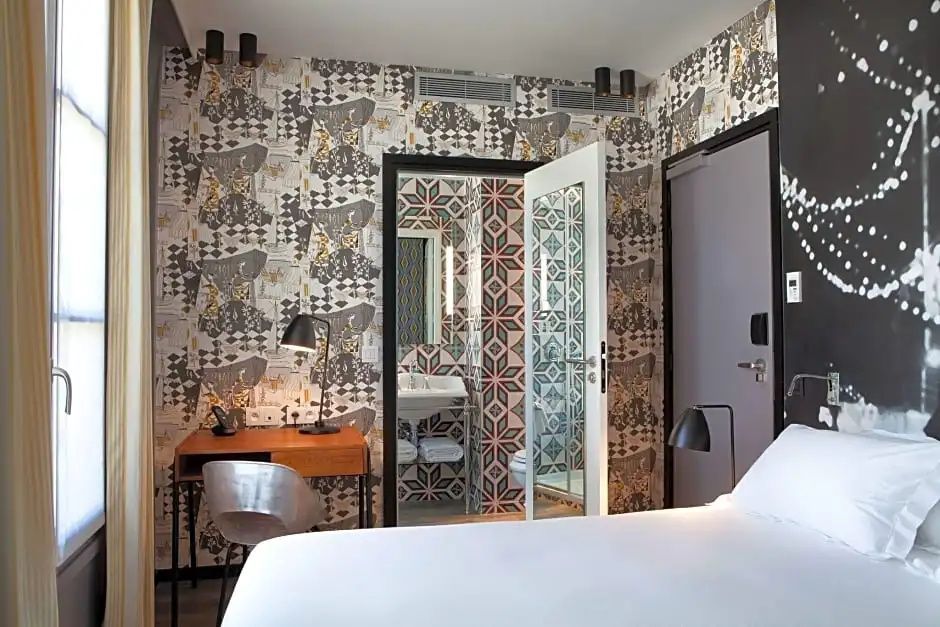 Zimmer mit gemusterter Tapete, Schreibtisch und geöffneter Tür zum bunten Badezimmer.