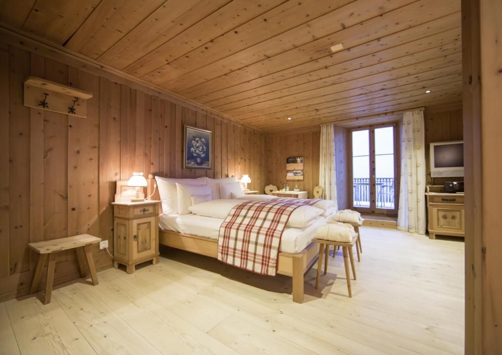 Hotelzimmer im alpinen Stil mit Holzvertäfelung, Doppelbett und Balkontür.