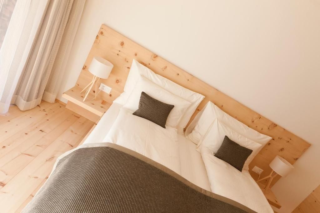 Doppelbett mit weißer Bettwäsche, dunklen Kissen und Kopfteil aus hellem Holz.
