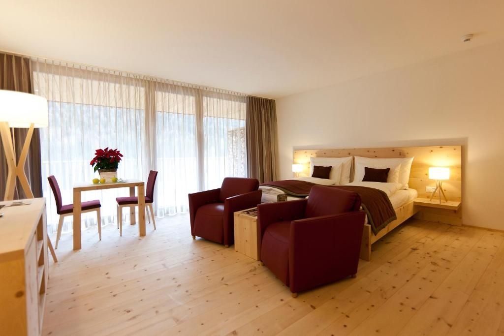 Helles Hotelzimmer mit Holzboden, zwei roten Sesseln und großer Fensterfront.