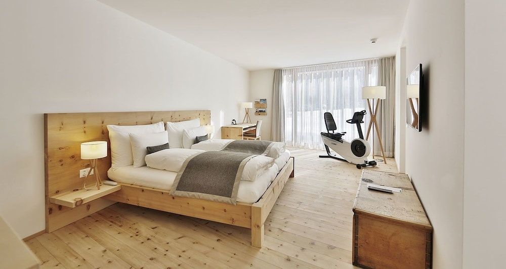 Schlafzimmer mit Doppelbett aus Holz, hellem Holzboden und Heimtrainer am Fenster.