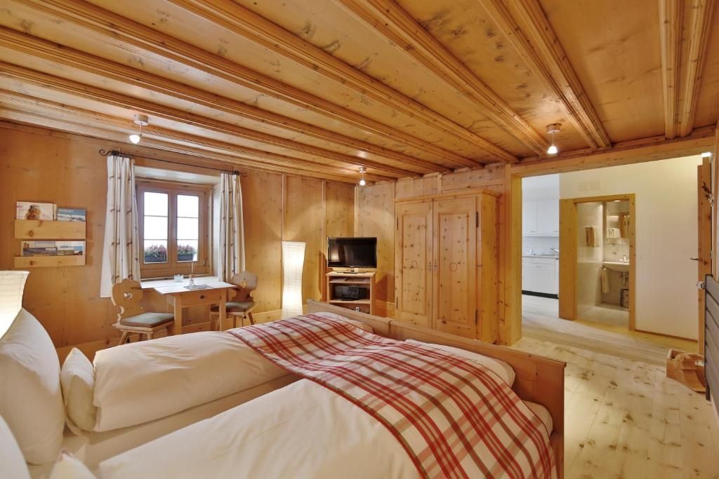 Hotelzimmer mit Holzbalkendecke, Doppelbett, Fernseher und Blick in den Nachbarraum