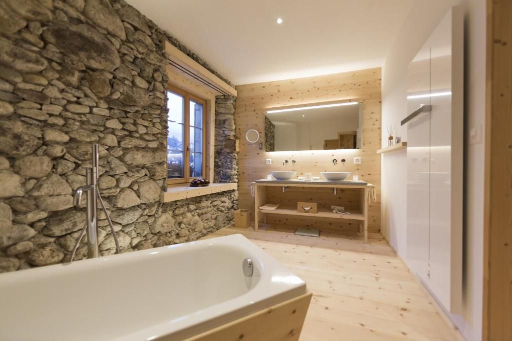 Badezimmer mit Natursteinwand, freistehender Badewanne und Doppelwaschtisch aus Holz