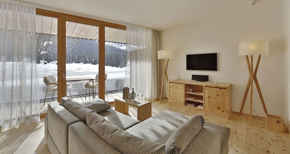 Wohnzimmer mit TV-Gerät auf Holzschrank, grauem Sofa und Aussicht auf den Schnee.