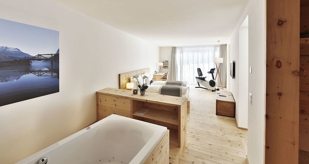 Helles Hotelzimmer mit Arvenholzmöbeln, integrierter Badewanne und Fitnessfahrrad.