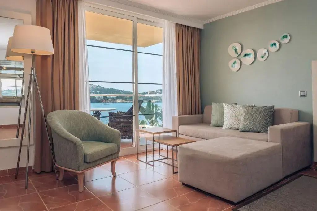 Wohnbereich einer Suite mit Sessel, Sofa, Hocker und großem Fenster mit Blick auf das Meer.