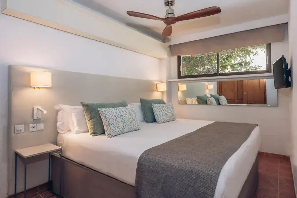 Doppelbett mit hellen Kissen und Deckenventilator in einem modern eingerichteten Hotelzimmer.