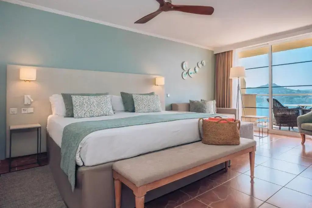 Helles Schlafzimmer der Suite mit Doppelbett, Sitzecke und Blick zum Balkon.