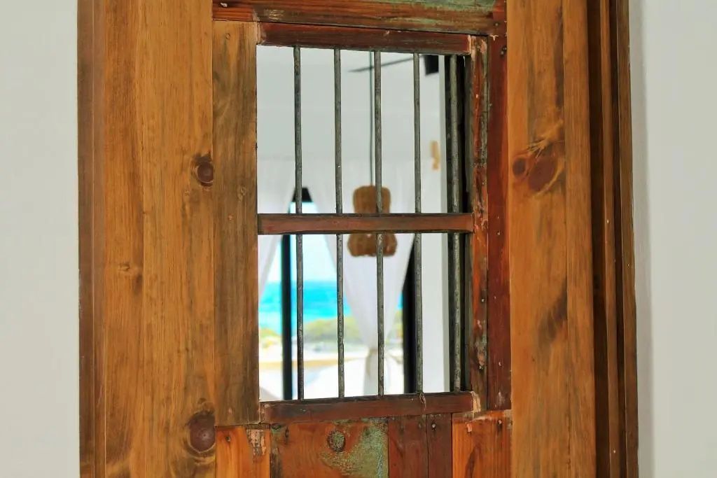 Blick durch ein rustikales Holzfenster auf das türkisblaue Meer im Hintergrund.