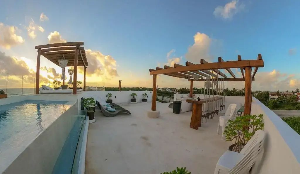 Dachterrasse mit Holzpergola, Barstühlen, Liegen und Blick auf den Abendhimmel.