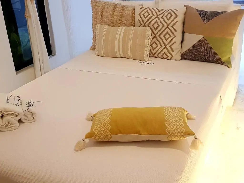 Doppelbett mit weißer Bettwäsche und gelbem Akzentkissen vor weißer Wand