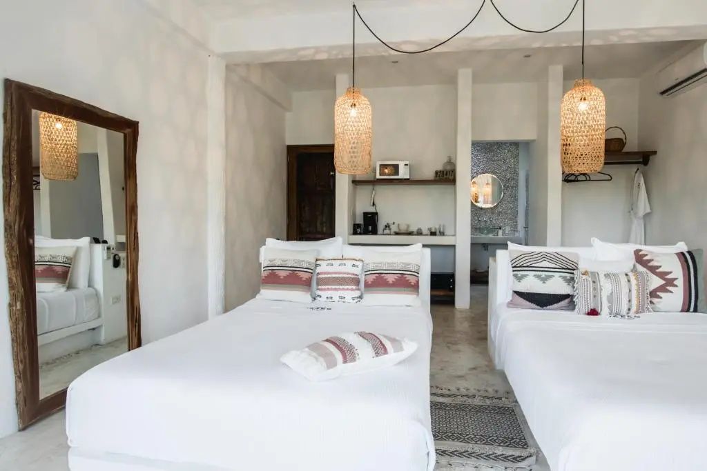 Helles Hotelzimmer mit zwei weißen Betten, Hängelampen aus Geflecht und Fliesenboden.
