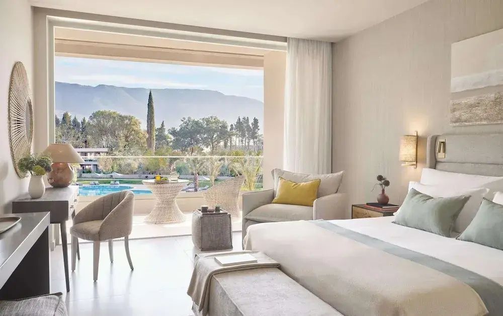 Blick aus dem Hotelzimmer über den Balkon auf eine Gartenanlage mit Pool und Berge im Hintergrund.