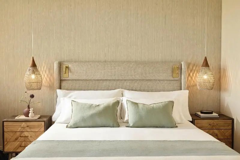 Doppelbett mit hellem Polster-Kopfteil, weissen Kissen und beigefarbener Wandbekleidung.