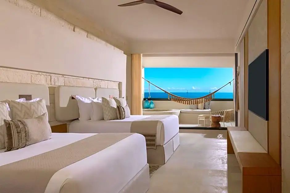 Schlafzimmer mit Betten und direktem Blick über den Balkon mit Hängematte auf das Meer.