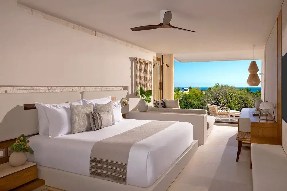 Hotelzimmer mit Doppelbett, Sitzbereich und offenem Balkon mit Blick aufs Meer.