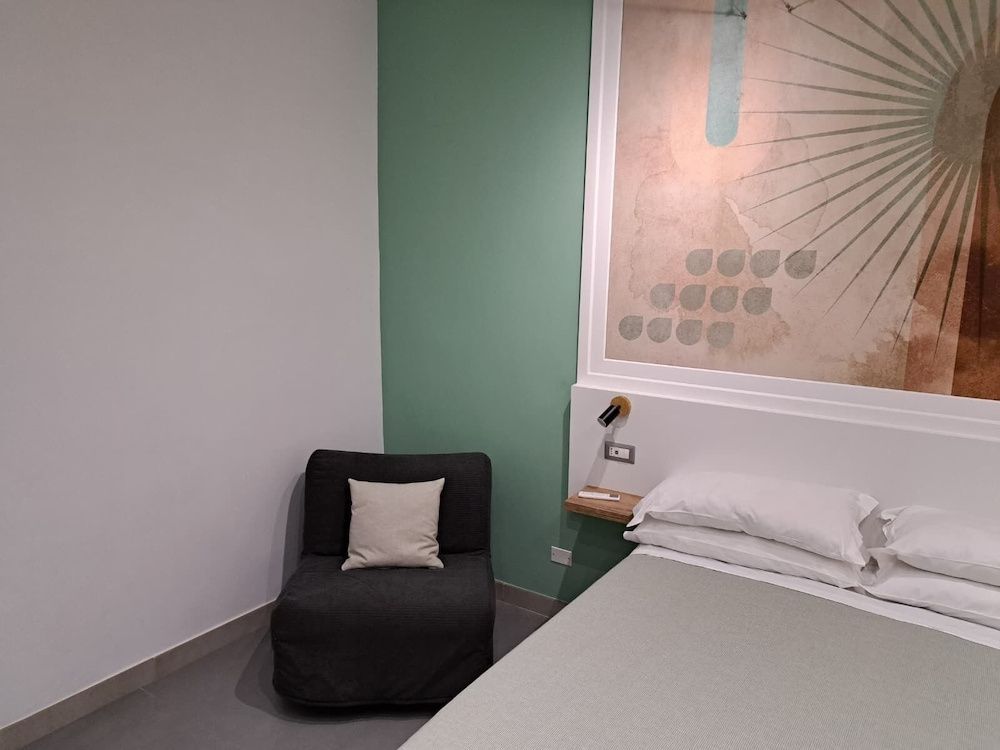 Modernes Hotelzimmer mit grün akzentuierter Wand, dunklem Sessel und Bett.