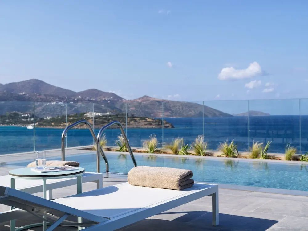 Liegestühle an einem Pool mit Aussicht auf das Meer und die gegenüberliegenden Berge.