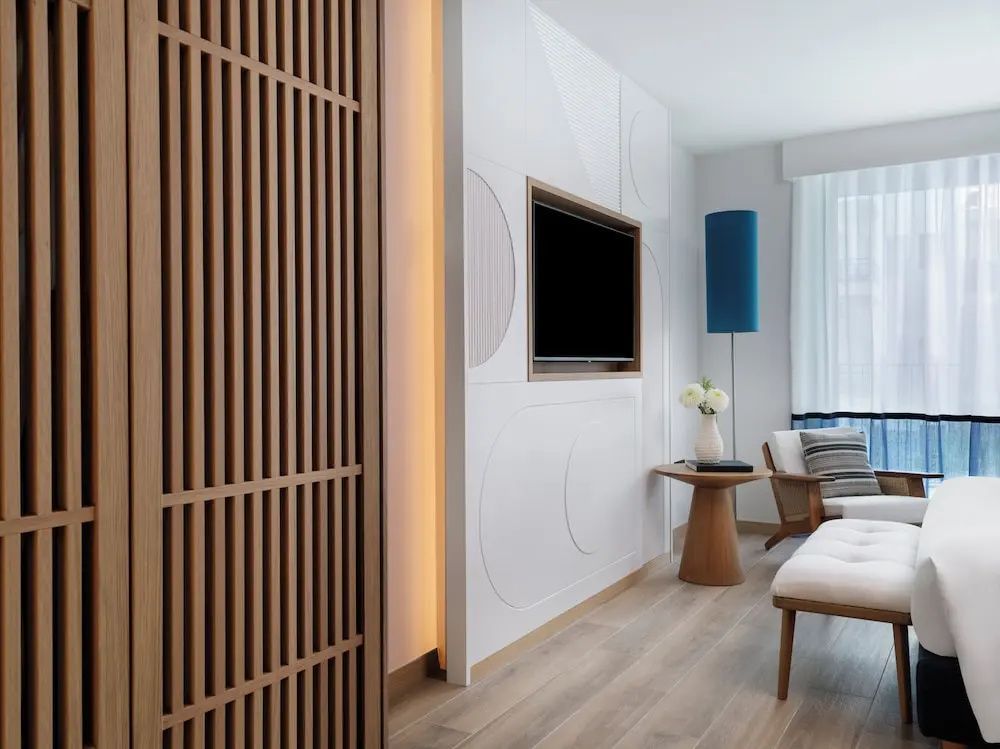 Wohnbereich im Hotelzimmer mit Flachbild-TV an der Wand und hölzernem Raumtrenner.