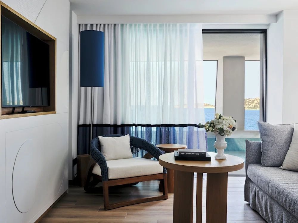 Sessel mit blauen Akzenten, kleiner Holztisch und Blick aufs Meer durch das Fenster.