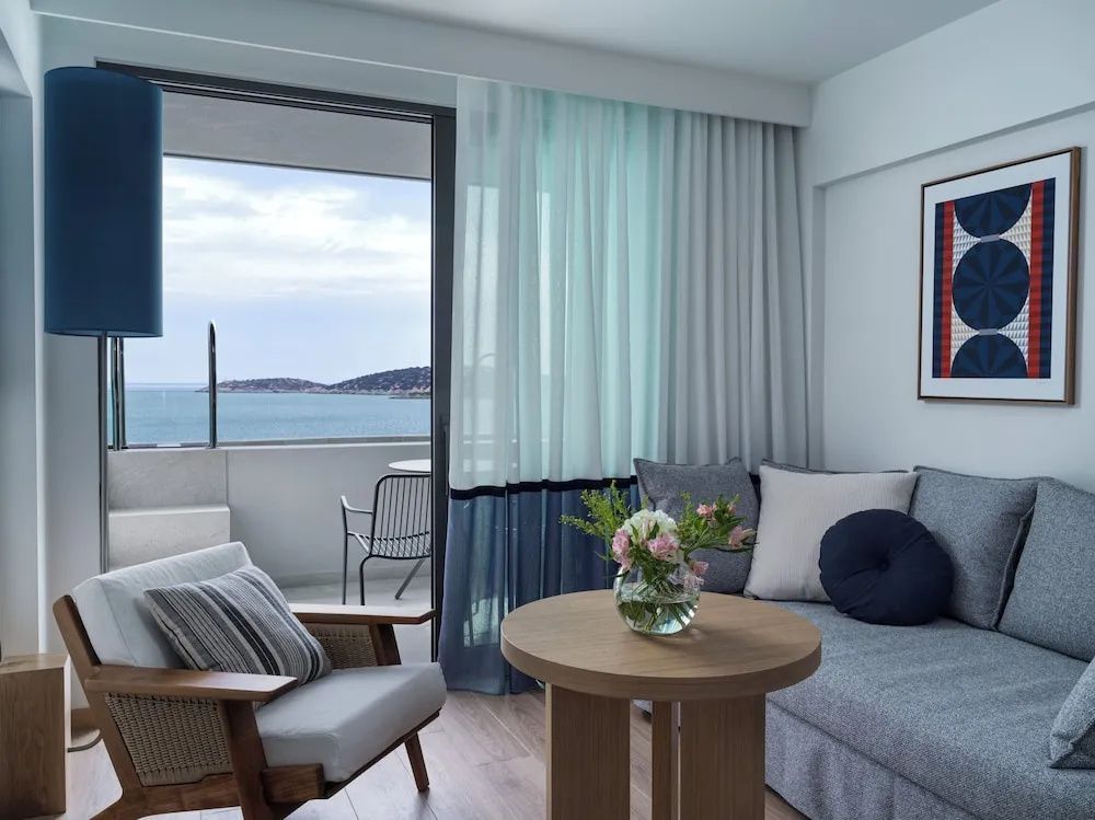 Sitzecke im Zimmer mit Sessel, Tisch und Vorhängen neben dem Balkon mit Meeresblick.