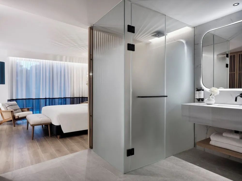 Gläserne Duschkabine und Waschtisch im Badezimmer mit Blick auf den Schlafbereich.