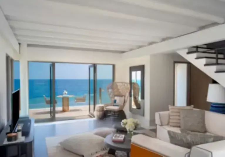 Geräumiges Wohnzimmer mit Sofa, Sessel und geöffneter Tür zur Terrasse mit Meerblick.