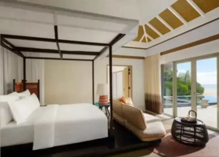 Schlafzimmer mit großem Bett, beigem Sofa und Blick durch die Glasschiebetür nach draußen.