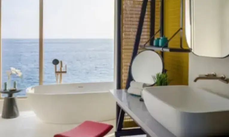 Badezimmer mit Waschtisch und einer Badewanne direkt am Fenster zum Meer.