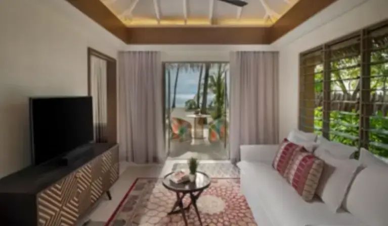 Heller Wohnbereich einer Villa mit weißem Sofa, Couchtisch und Blick auf Palmen und Strand.