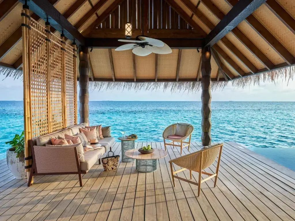 Überdachte Holzterrasse über dem Wasser mit Sitzmöbeln und freiem Blick auf das Meer.